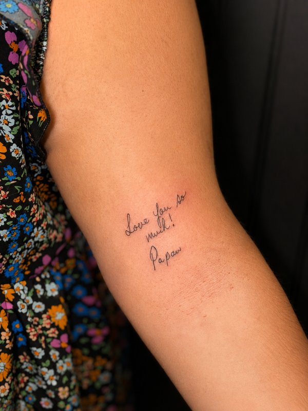 Fine-line tattoo recreating a loved one's handwriting on an upper arm
