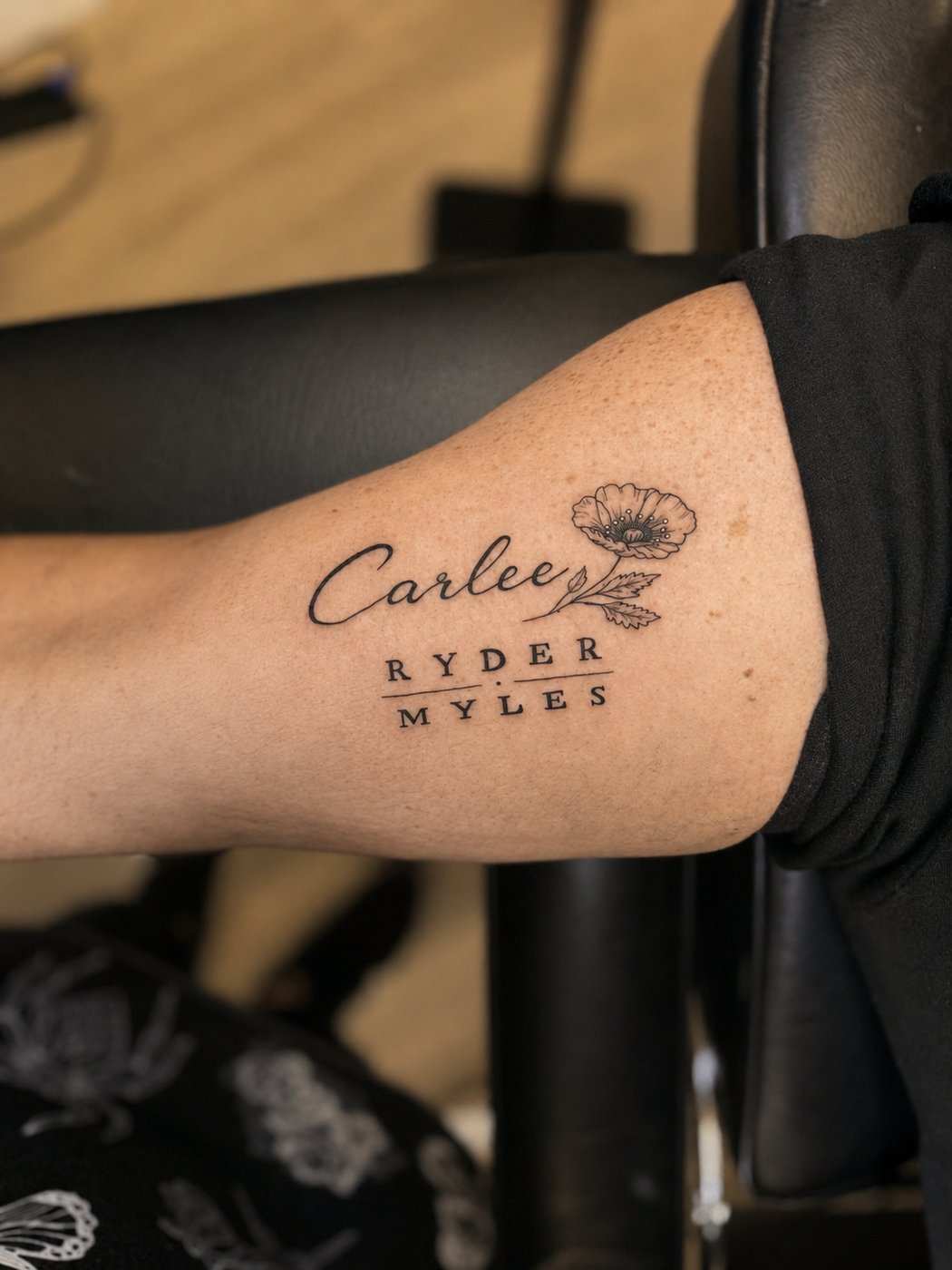 Tattoo mixing script and serif lettering of family names beside a small poppy